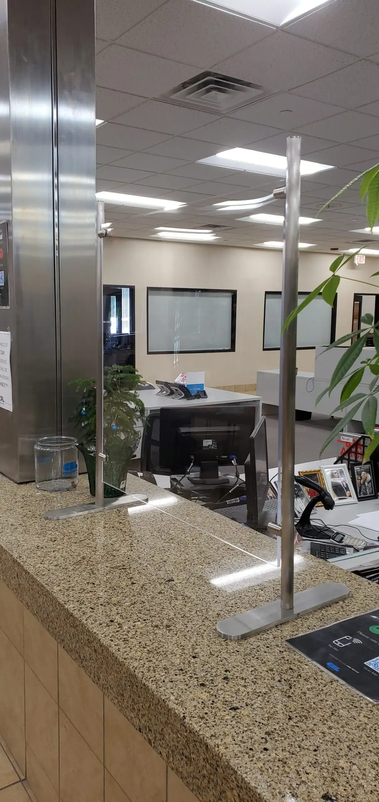 Freestanding clear glass countertop barrier at a commercial desk.