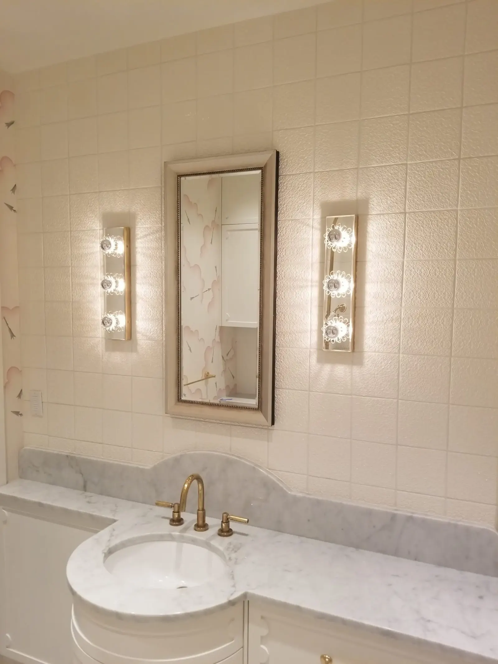 Bathroom wall mirror installed between vertical light sconces.